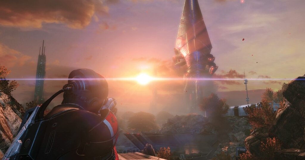 Comandante Shepard, de armadura N7 com a faixa vermelha, observa ao pôr do sol a gigantesca nave Sovereign pousada no horizonte de Eden Prime, em cena de Mass Effect Legendary Edition