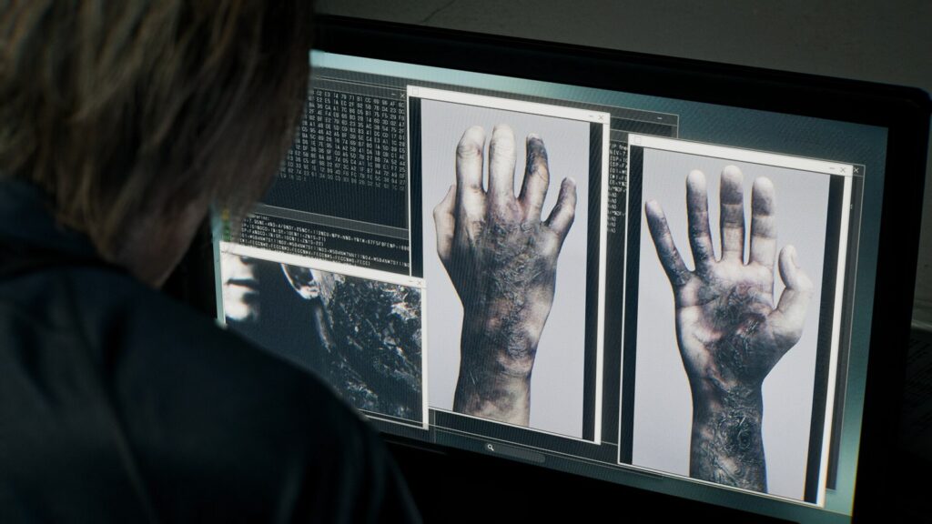 Personagem de costas analisa fotos de mãos infectadas e linhas de código na tela de um computador, em captura oficial de Resident Evil Requiem