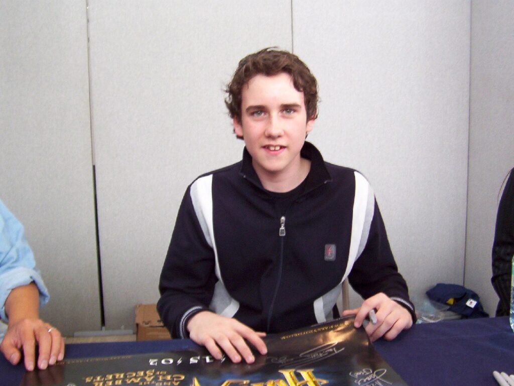 Matthew Lewis aos 14 anos, sentado a uma mesa de autógrafos em 2003