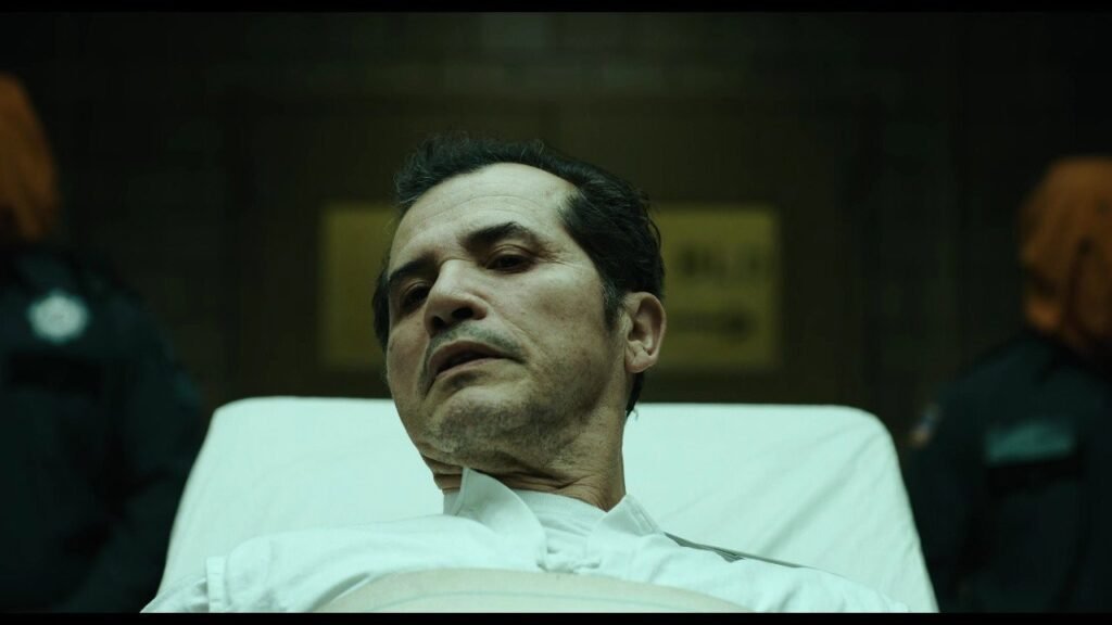 John Leguizamo deitado numa maca, cercado por guardas, em O Exorcista: Mártires