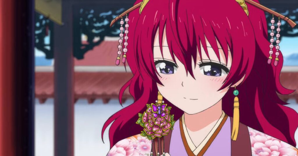 A princesa Yona, de cabelo vermelho, com enfeites dourados no cabelo, segura um grampo de cabelo enfeitado com flores e sorri no pátio do palácio real de Kouka, em cena do anime Yona of the Dawn