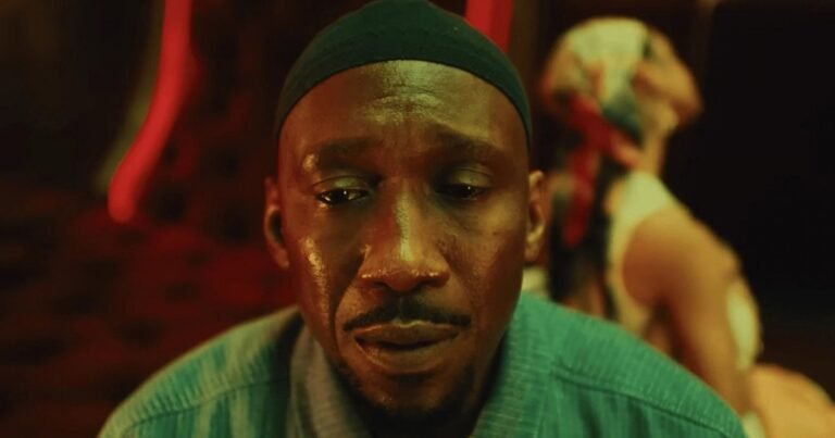 Mahershala Ali, de gorro verde, em close sob luz vermelha em Your Mother Your Mother Your Mother